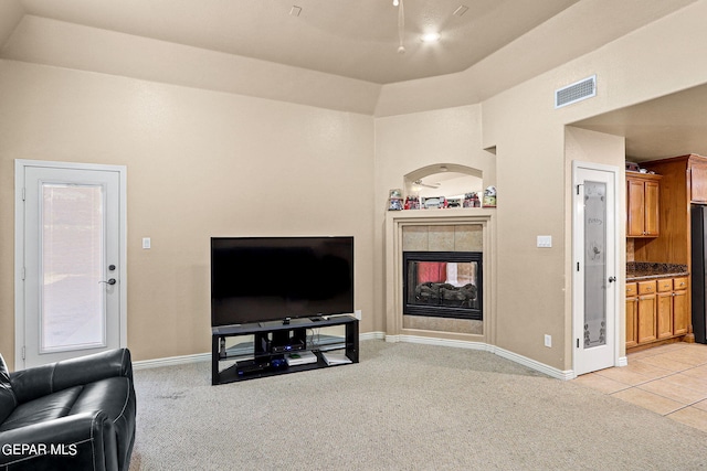 living room with a tiled fireplace, lofted ceiling, and light colored carpet