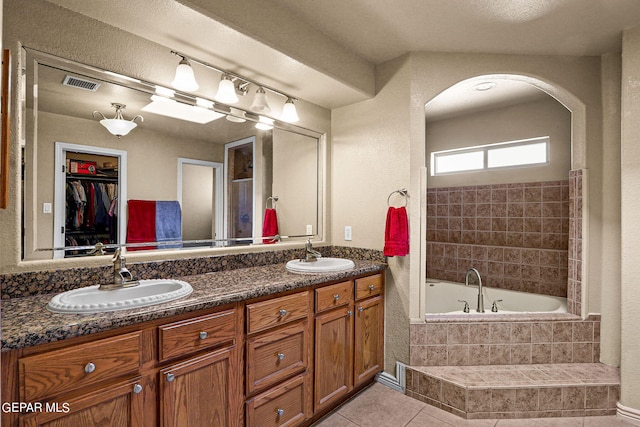 bathroom with a relaxing tiled tub, vanity, and tile patterned flooring