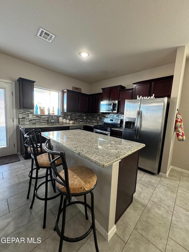 kitchen featuring tasteful backsplash, a breakfast bar area, a center island, stainless steel appliances, and light stone countertops