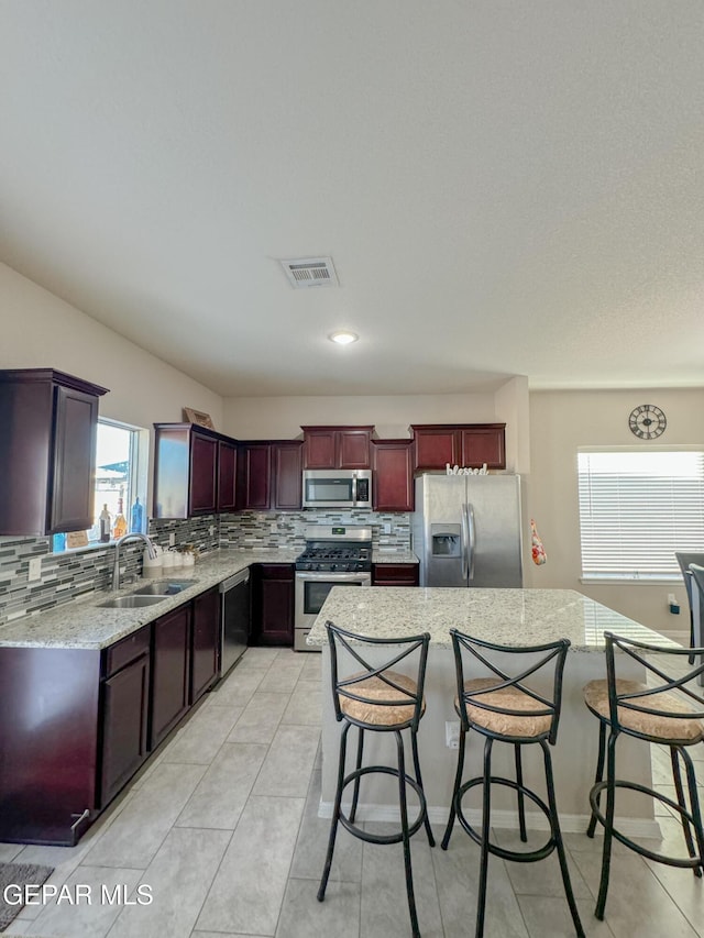 kitchen with sink, a breakfast bar, appliances with stainless steel finishes, a center island, and tasteful backsplash