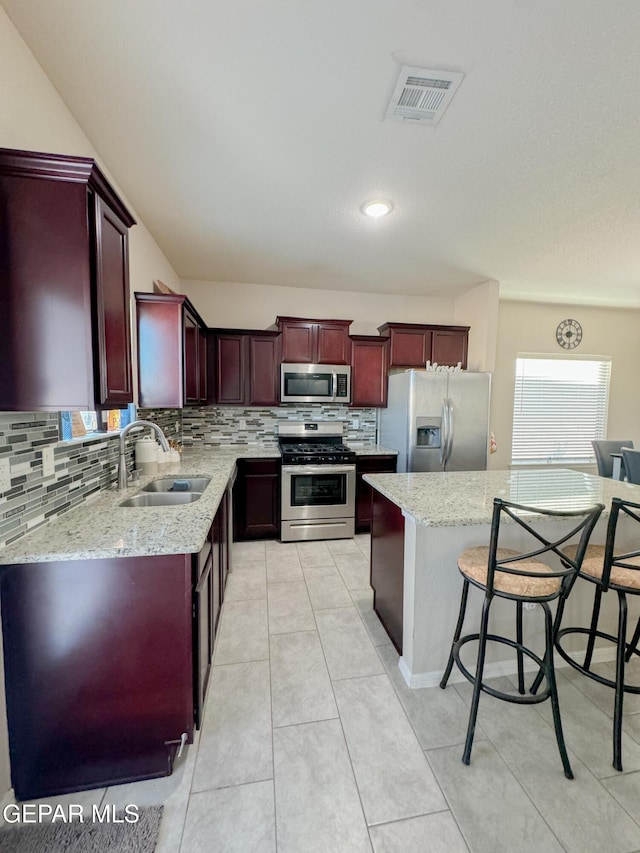 kitchen featuring sink, appliances with stainless steel finishes, backsplash, a center island, and light stone countertops