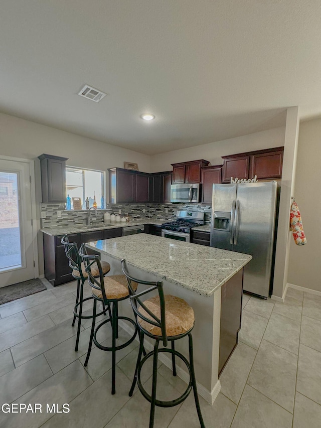 kitchen featuring a breakfast bar area, appliances with stainless steel finishes, backsplash, light stone counters, and a kitchen island