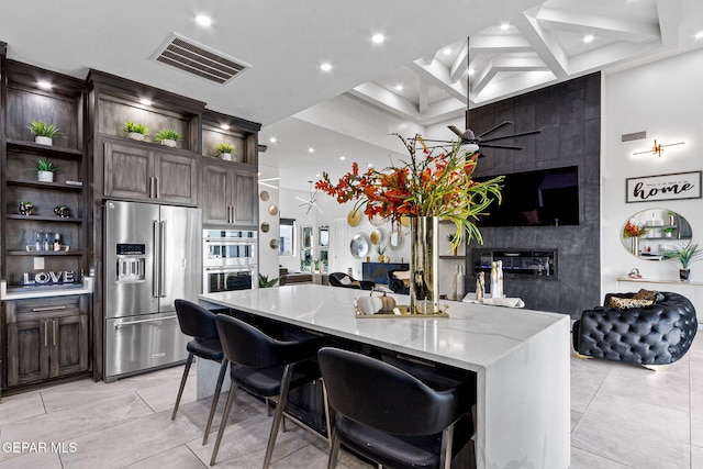 kitchen with dark brown cabinets, stainless steel appliances, a breakfast bar, and light stone countertops