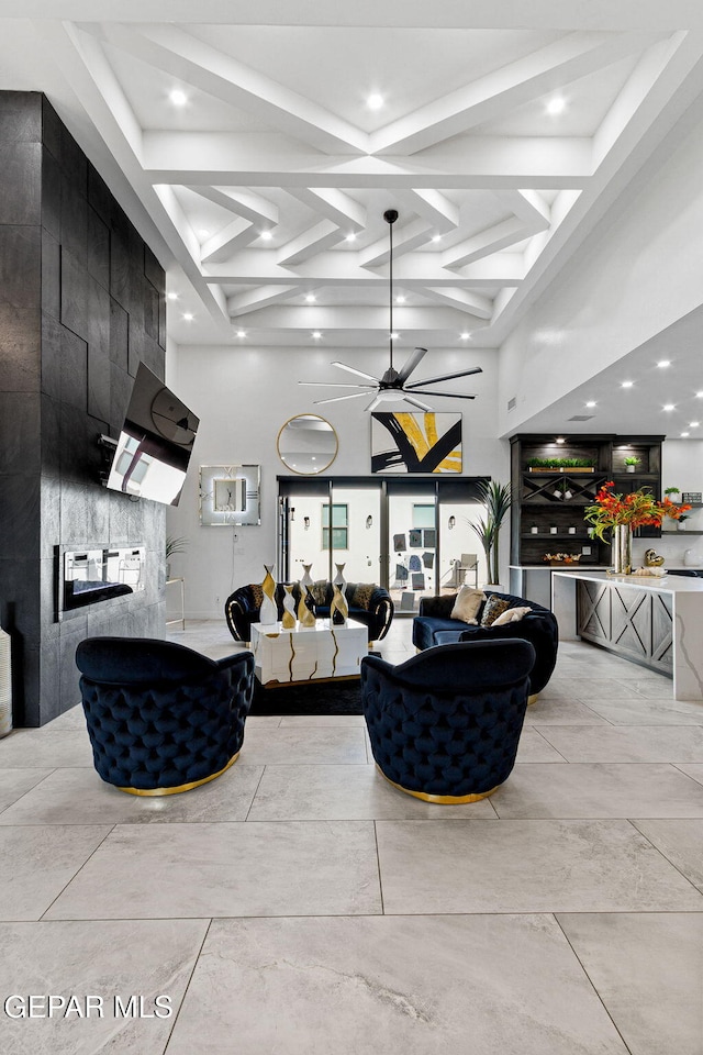 living room featuring ceiling fan, a towering ceiling, beam ceiling, coffered ceiling, and a large fireplace