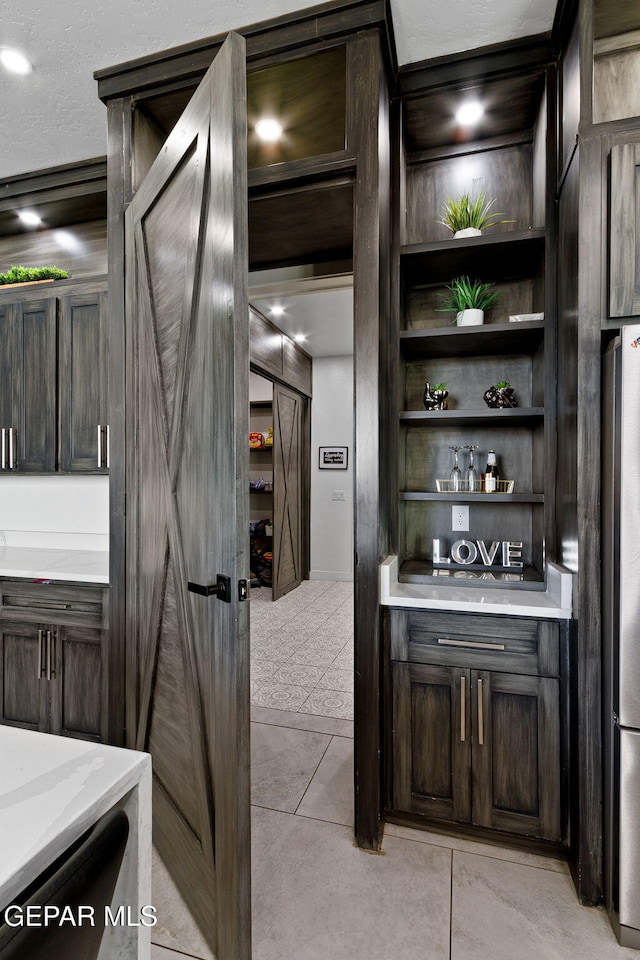 interior space featuring light tile patterned flooring, dark brown cabinets, and stainless steel refrigerator