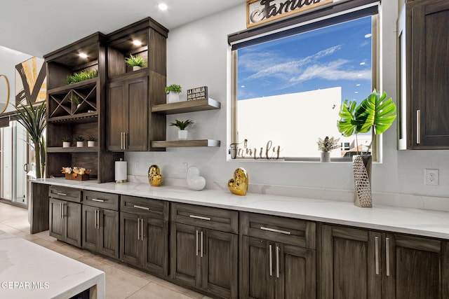 bar featuring dark brown cabinetry, light stone countertops, and light tile patterned floors