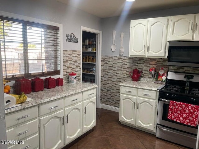 kitchen featuring stainless steel appliances, white cabinetry, light stone countertops, and dark tile patterned floors