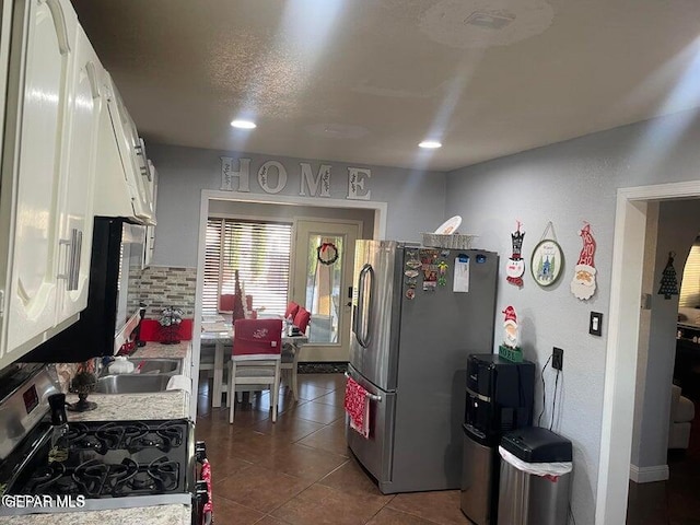 kitchen with sink, white cabinets, appliances with stainless steel finishes, dark tile patterned floors, and backsplash