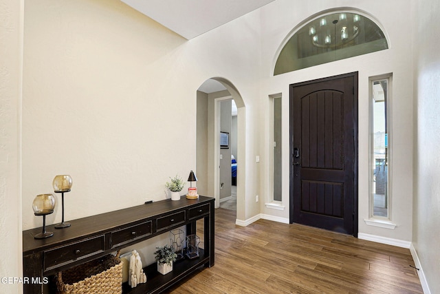 foyer featuring baseboards, arched walkways, and wood finished floors