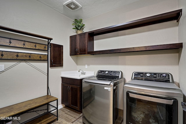 clothes washing area with a sink, a textured ceiling, cabinet space, separate washer and dryer, and light wood finished floors