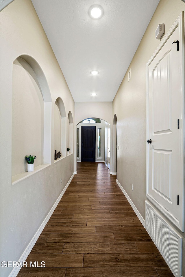 hallway featuring visible vents, baseboards, arched walkways, and dark wood-style flooring