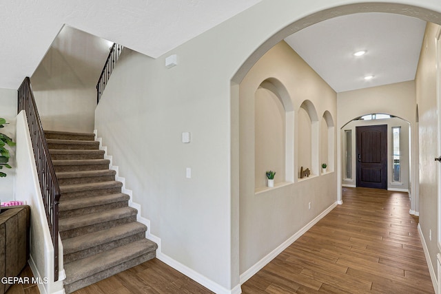 foyer with wood finished floors, recessed lighting, arched walkways, baseboards, and stairs