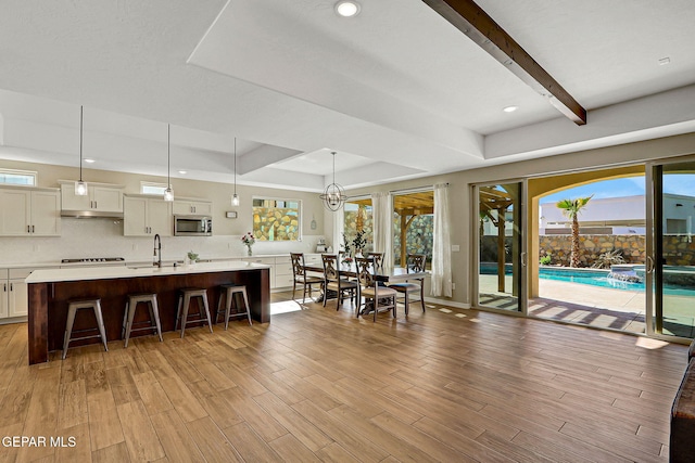 interior space with a sink, a tray ceiling, stainless steel microwave, a breakfast bar area, and light countertops