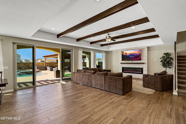 living area with ceiling fan, stairway, beam ceiling, wood finished floors, and a glass covered fireplace