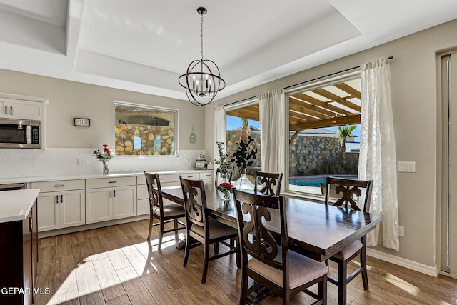 dining area featuring a raised ceiling, a notable chandelier, and light wood-style flooring