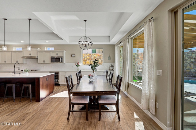 dining space featuring light wood-style flooring, baseboards, an inviting chandelier, and beverage cooler