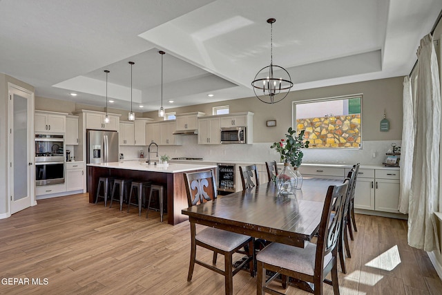 dining space with recessed lighting, a tray ceiling, an inviting chandelier, and light wood finished floors