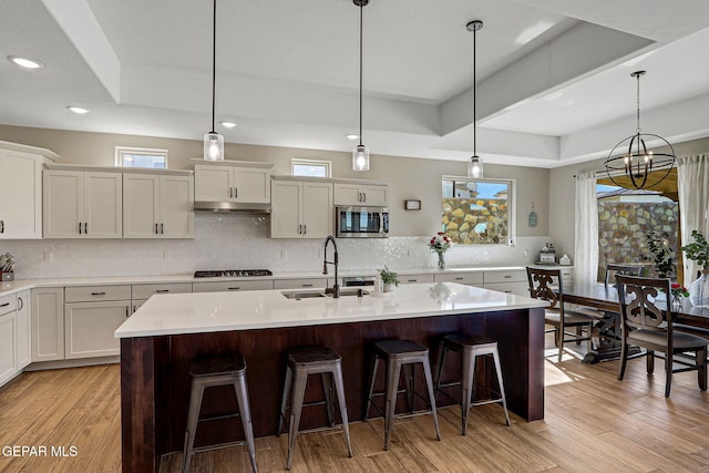 kitchen with light wood-type flooring, a sink, stainless steel microwave, gas cooktop, and under cabinet range hood