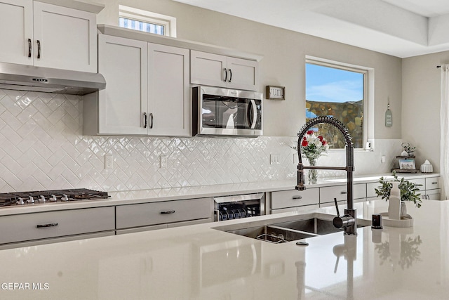 kitchen with a sink, decorative backsplash, light countertops, stainless steel appliances, and under cabinet range hood