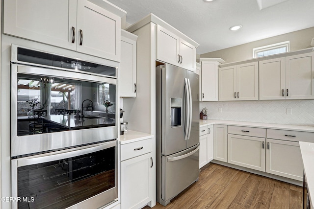 kitchen featuring light wood-type flooring, stainless steel appliances, backsplash, and white cabinets