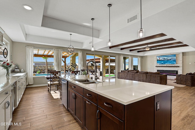 kitchen featuring visible vents, a sink, light countertops, a glass covered fireplace, and a raised ceiling