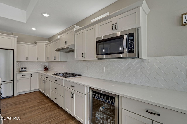 kitchen featuring beverage cooler, under cabinet range hood, light countertops, wood finished floors, and stainless steel appliances