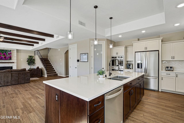 kitchen featuring light wood finished floors, a tray ceiling, a fireplace, stainless steel appliances, and a sink