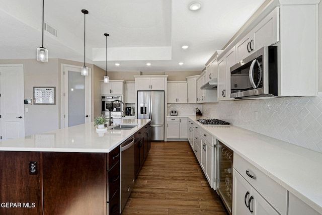 kitchen with a sink, dark wood-type flooring, under cabinet range hood, appliances with stainless steel finishes, and backsplash