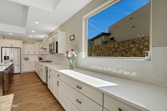 kitchen with light wood-style flooring, backsplash, white cabinetry, appliances with stainless steel finishes, and light countertops