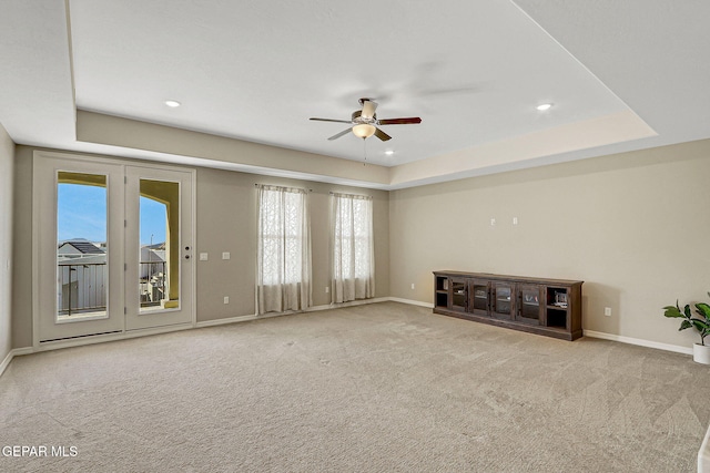 unfurnished living room with a wealth of natural light, a raised ceiling, carpet floors, and a ceiling fan