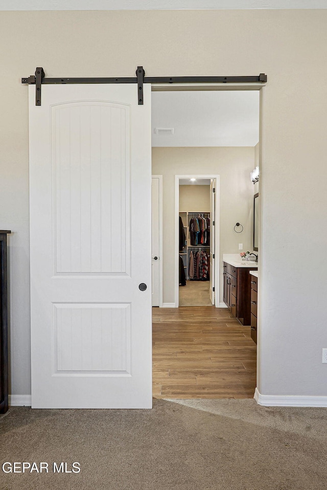 interior space with visible vents, baseboards, a barn door, light carpet, and light wood-style flooring