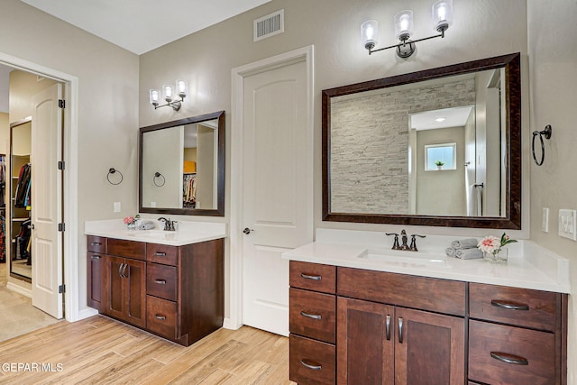 bathroom featuring a spacious closet, visible vents, two vanities, wood finished floors, and a sink