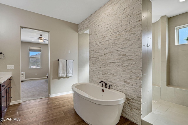 full bathroom featuring a ceiling fan, wood finished floors, baseboards, a freestanding bath, and vanity