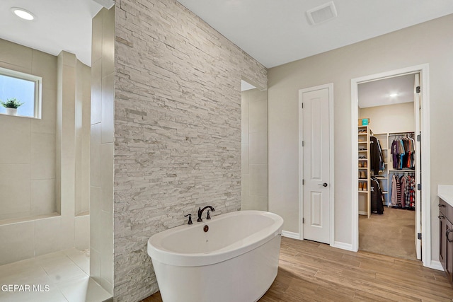 bathroom featuring a walk in closet, a soaking tub, wood finished floors, and a walk in shower