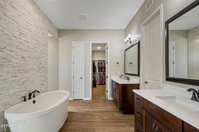 bathroom with a freestanding tub, wood finished floors, visible vents, and a sink