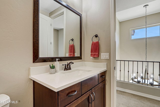 bathroom with toilet, vanity, baseboards, and a textured wall