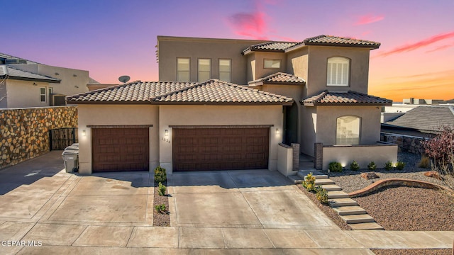 mediterranean / spanish home with a tiled roof, an attached garage, driveway, and stucco siding