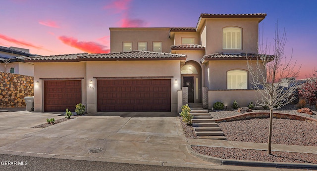 mediterranean / spanish home with a tile roof, concrete driveway, a garage, and stucco siding