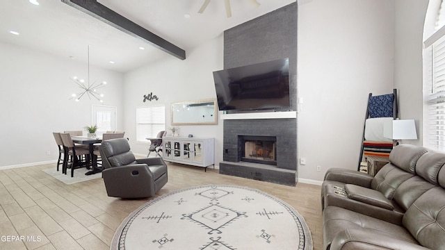 living room with ceiling fan with notable chandelier, beamed ceiling, a high ceiling, a brick fireplace, and light wood-type flooring