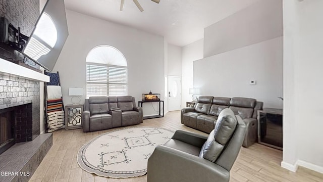 living room featuring ceiling fan, a brick fireplace, a towering ceiling, and light hardwood / wood-style floors