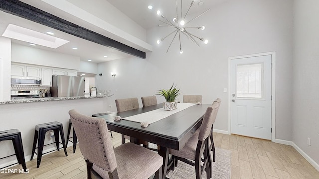 dining space featuring sink, beam ceiling, a chandelier, and light hardwood / wood-style floors