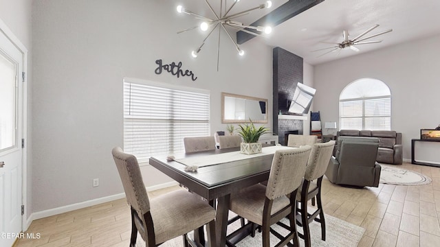 dining room with ceiling fan with notable chandelier, a fireplace, and light hardwood / wood-style floors