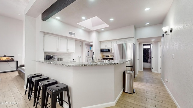 kitchen featuring appliances with stainless steel finishes, white cabinetry, a kitchen bar, light stone counters, and kitchen peninsula