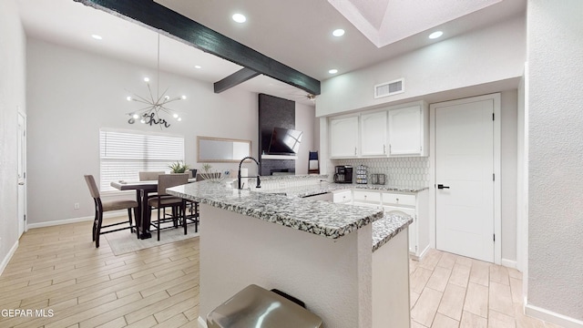 kitchen with tasteful backsplash, white cabinetry, light stone counters, kitchen peninsula, and beam ceiling