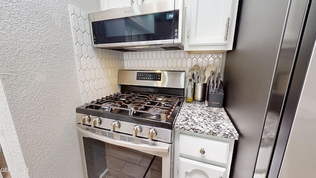 kitchen featuring stainless steel appliances, white cabinetry, backsplash, and light stone counters