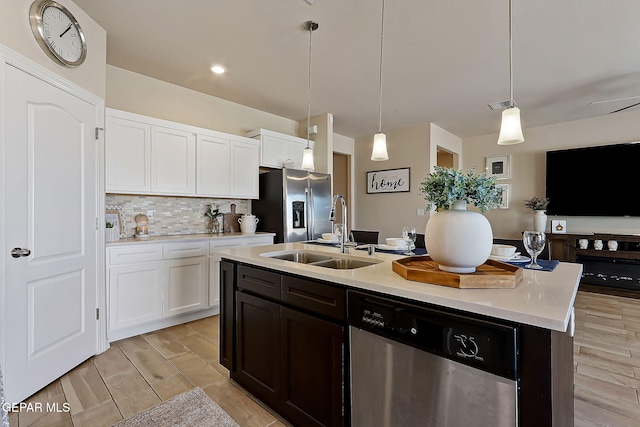 kitchen with sink, appliances with stainless steel finishes, pendant lighting, a kitchen island with sink, and white cabinets