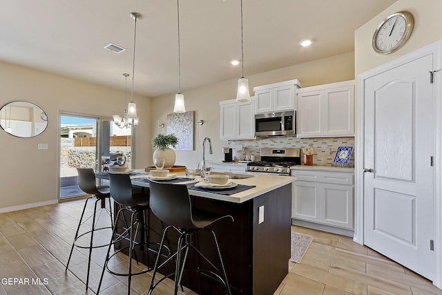 kitchen featuring sink, appliances with stainless steel finishes, white cabinetry, an island with sink, and decorative light fixtures