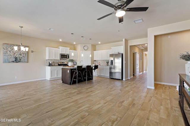 kitchen with decorative light fixtures, an island with sink, white cabinetry, a breakfast bar area, and stainless steel appliances