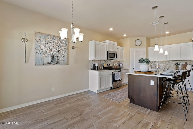 kitchen featuring a kitchen bar, decorative light fixtures, stainless steel appliances, a kitchen island with sink, and white cabinets