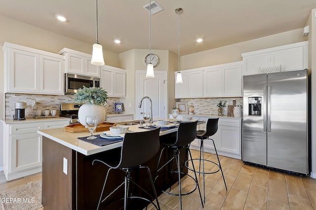 kitchen featuring stainless steel appliances, a center island with sink, pendant lighting, and white cabinets